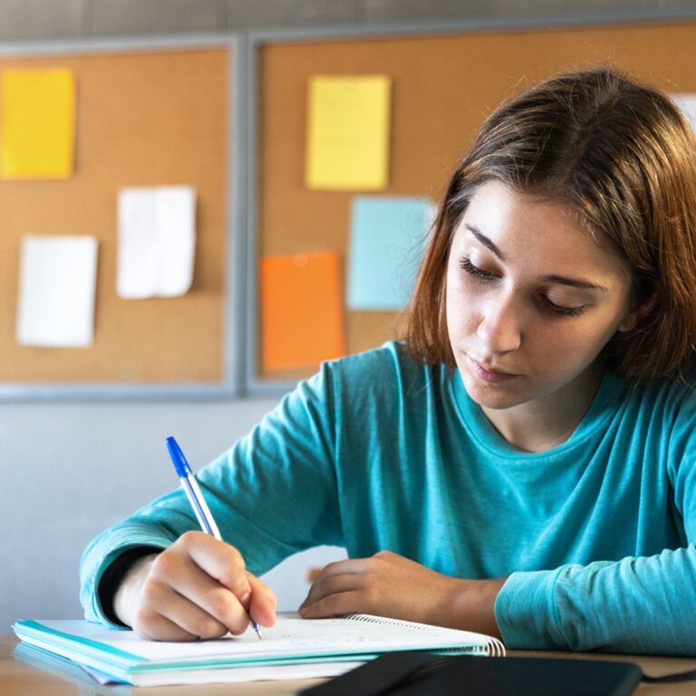 Menina estudando sobre o uso dos porquês: por que, por quê, porque ou porquê. Ela está concentrada escrevendo em um caderno, ilustrando a importância de entender as diferenças e os usos corretos dessas palavras na língua portuguesa.