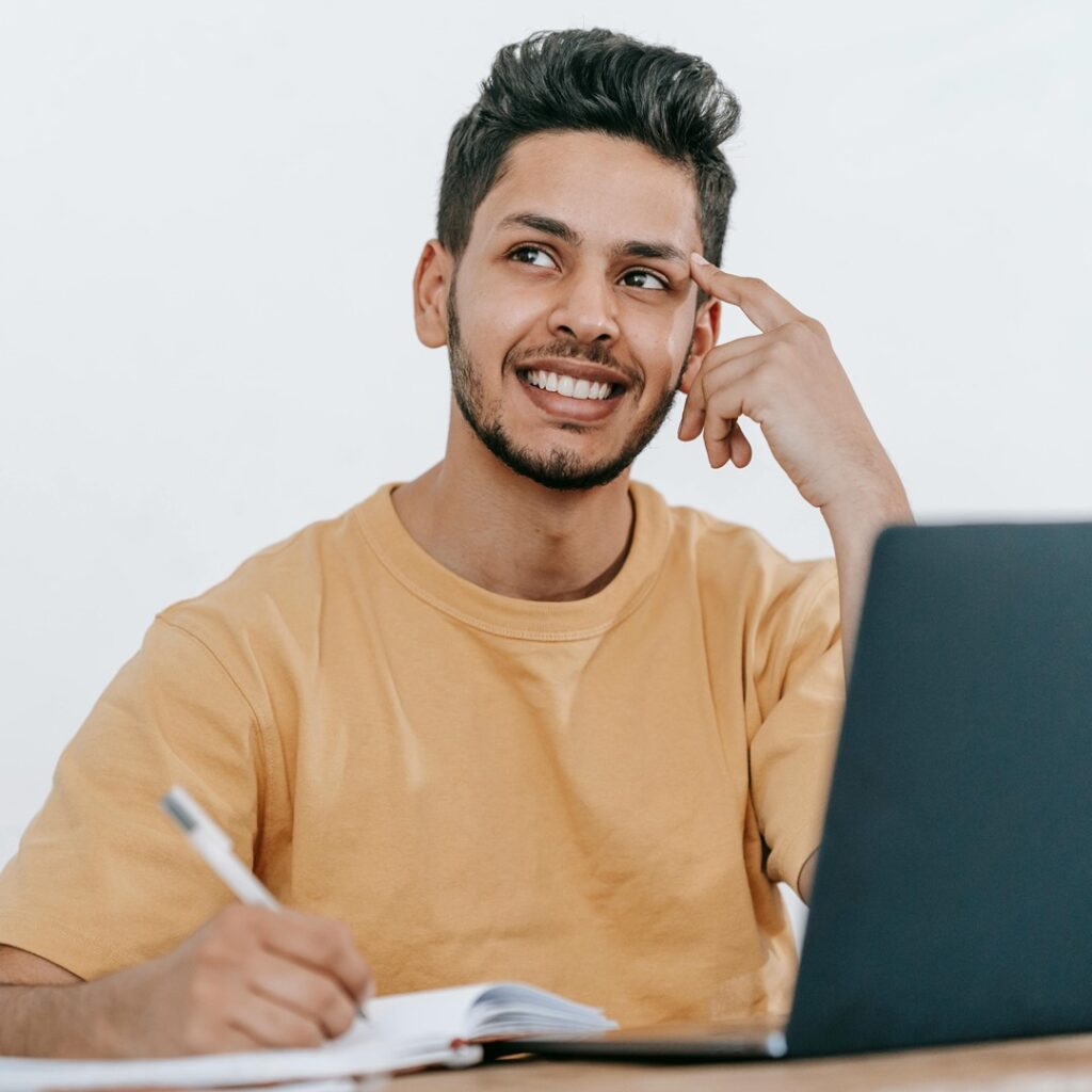 Estudante sorridente fazendo anotações e usando um laptop, representando a pesquisa sobre como funciona o SiSu, o Sistema de Seleção Unificada para ingresso em universidades públicas.