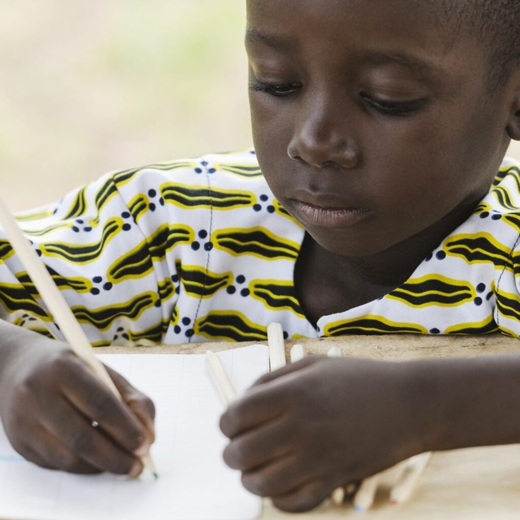 Criança negra escrevendo em um caderno, representando o tema redação sobre racismo no Brasil, destacando a importância de abordar a igualdade racial e a conscientização nas escolas.