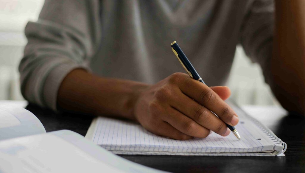 Pessoa escrevendo em um caderno, representando o processo de preparação e escrita da redação da Fuvest para o vestibular.