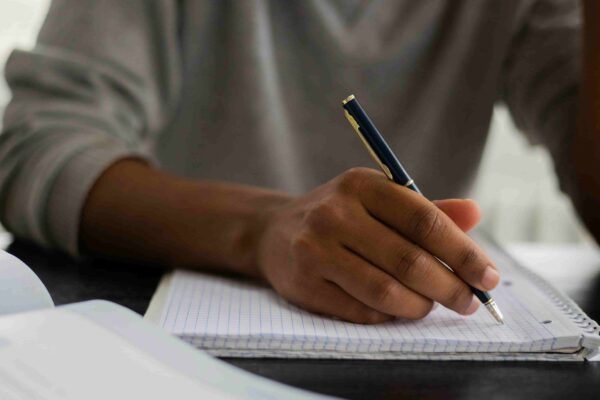 Pessoa escrevendo em um caderno, representando o processo de preparação e escrita da redação da Fuvest para o vestibular.