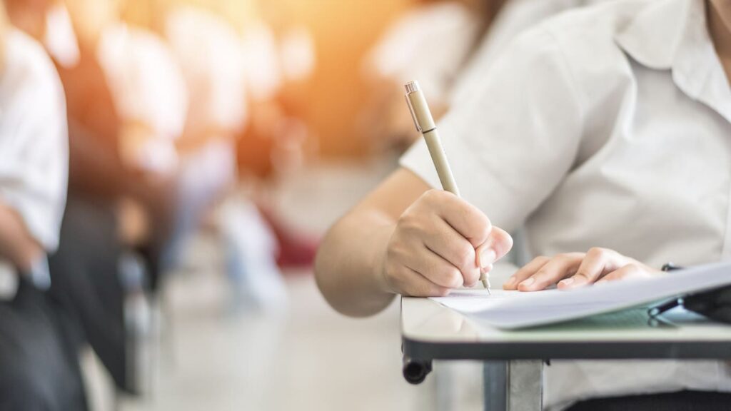 Estudante escrevendo em um papel durante o 'Primeiro dia Enem', simbolizando a concentração e preparação para o exame.