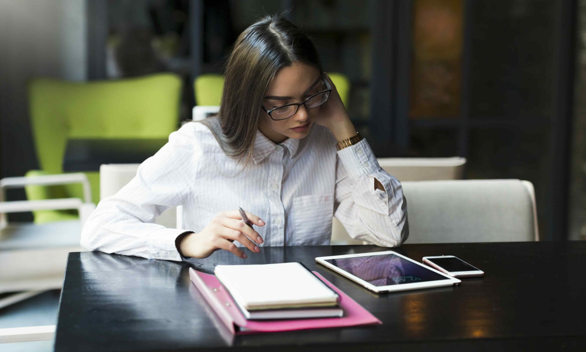 Estudante da faculdade de administração estudando sozinha em um café, com tablet, caderno e smartphone sobre a mesa.