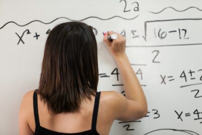 Estudante resolvendo questões de matemática em um quadro branco, se preparando para a segunda fase do vestibular.