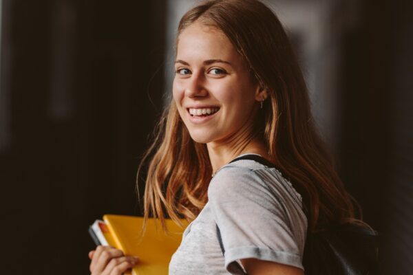 Estudante sorridente segurando cadernos, representando organização e motivação para seguir um plano de estudos eficaz.