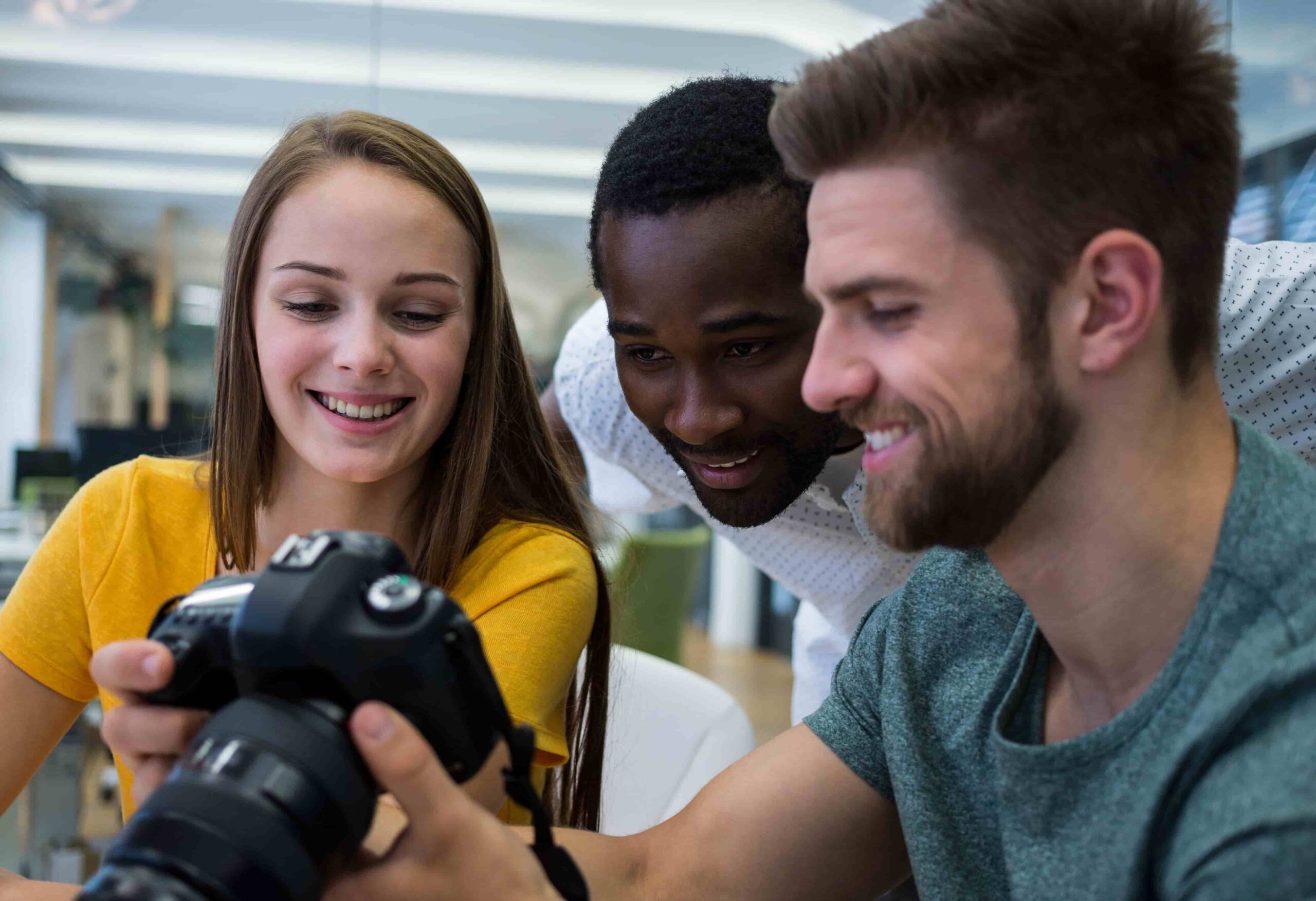 Três estudantes de Publicidade e Propaganda analisam juntos o visor de uma câmera. A imagem transmite colaboração, criatividade e entusiasmo, com foco em projetos de fotografia ou marketing visual.