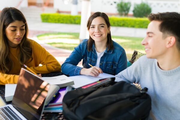 Grupo de estudantes estudando ao ar livre para o Vestibular Unicamp, com livros, cadernos e notebooks.