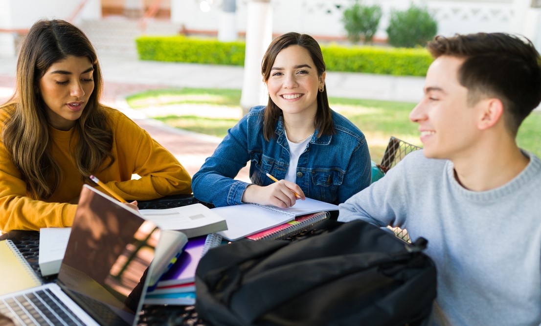 Grupo de estudantes estudando ao ar livre para o Vestibular Unicamp, com livros, cadernos e notebooks.