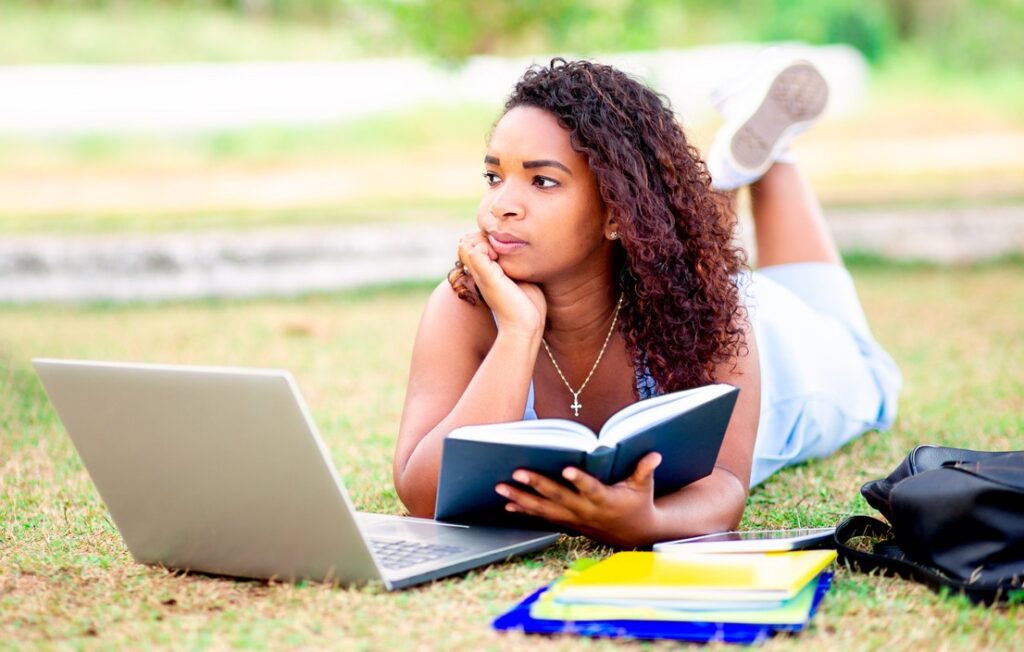 Estudante ao ar livre, com livro e notebook, revisando conteúdos de Linguagens, Códigos e suas Tecnologias para o Enem.