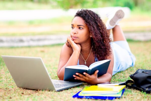 Estudante ao ar livre, com livro e notebook, revisando conteúdos de Linguagens, Códigos e suas Tecnologias para o Enem.