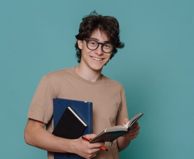 Jovem estudante sorridente segurando cadernos e caneta, representando um treineiro Enem se preparando para a prova.