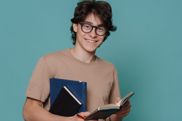 Jovem estudante sorridente segurando cadernos e caneta, representando um treineiro Enem se preparando para a prova.