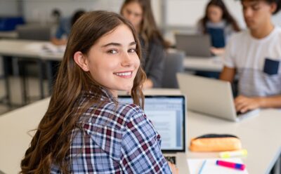 Estudante sorridente em sala de aula usando um notebook, representando o processo de como se inscrever no Enem e se preparar para a prova