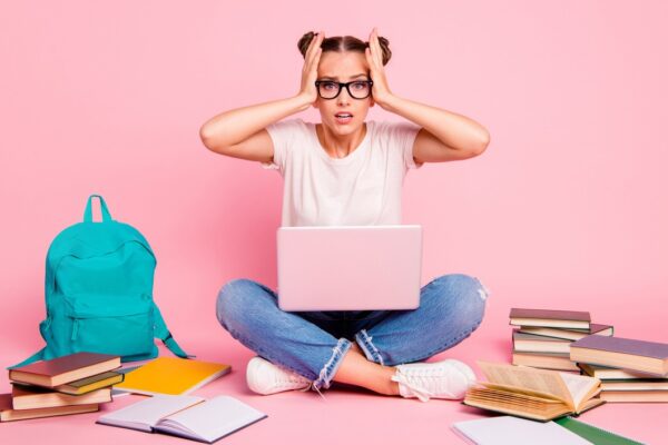 Estudante estressada com notebook e livros ao redor, representando a pressão e desafios de estudar para o vestibular e se preparar para a prova.
