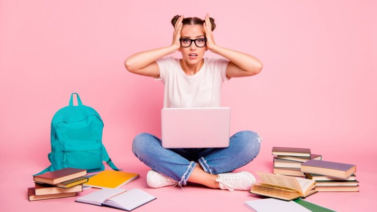 Estudante estressada com notebook e livros ao redor, representando a pressão e desafios de estudar para o vestibular e se preparar para a prova.