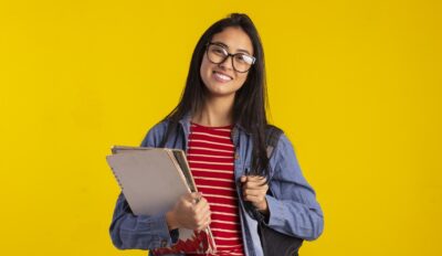 Estudante segurando apostilas e uma mochila em referencia à prática de simulado de vestibulares para a preparação.