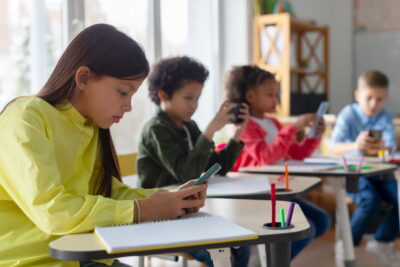 Alunos em sala de aula usando celulares e cadernos para pesquisar e estudar atualidades no Enem, desenvolvendo conhecimentos atualizados para a prova.