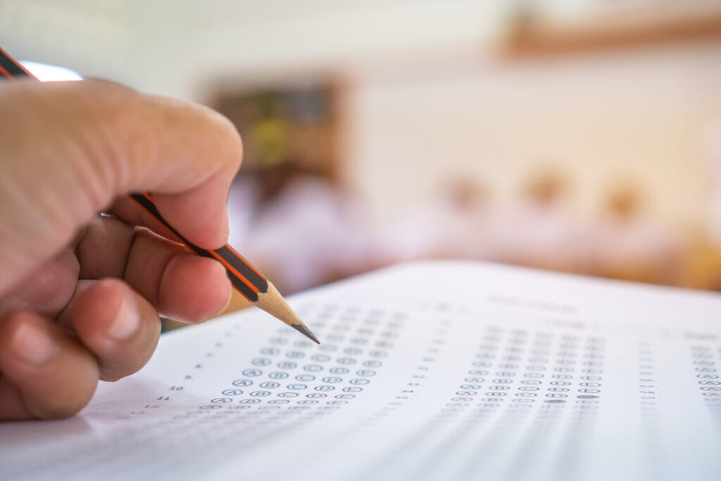 Mão preenchendo cartão de respostas em simulado, representando o Boletim de Desempenho Enem como ferramenta essencial para avaliar a performance do estudante.