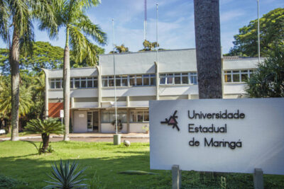 Fachada da Universidade Estadual de Maringá com placa institucional, destacando o Vestibular UEM como porta de entrada para cursos de graduação.