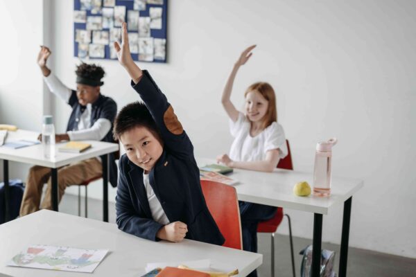 Alunos levantando a mão durante uma aula em sala de aula, ilustrando o aprendizado da língua portuguesa e a diferença entre a fim ou afim, uma das dúvidas mais comuns de ortografia e gramática.