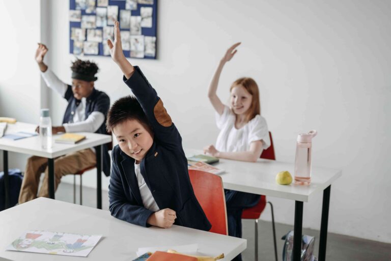 Alunos levantando a mão durante uma aula em sala de aula, ilustrando o aprendizado da língua portuguesa e a diferença entre a fim ou afim, uma das dúvidas mais comuns de ortografia e gramática.