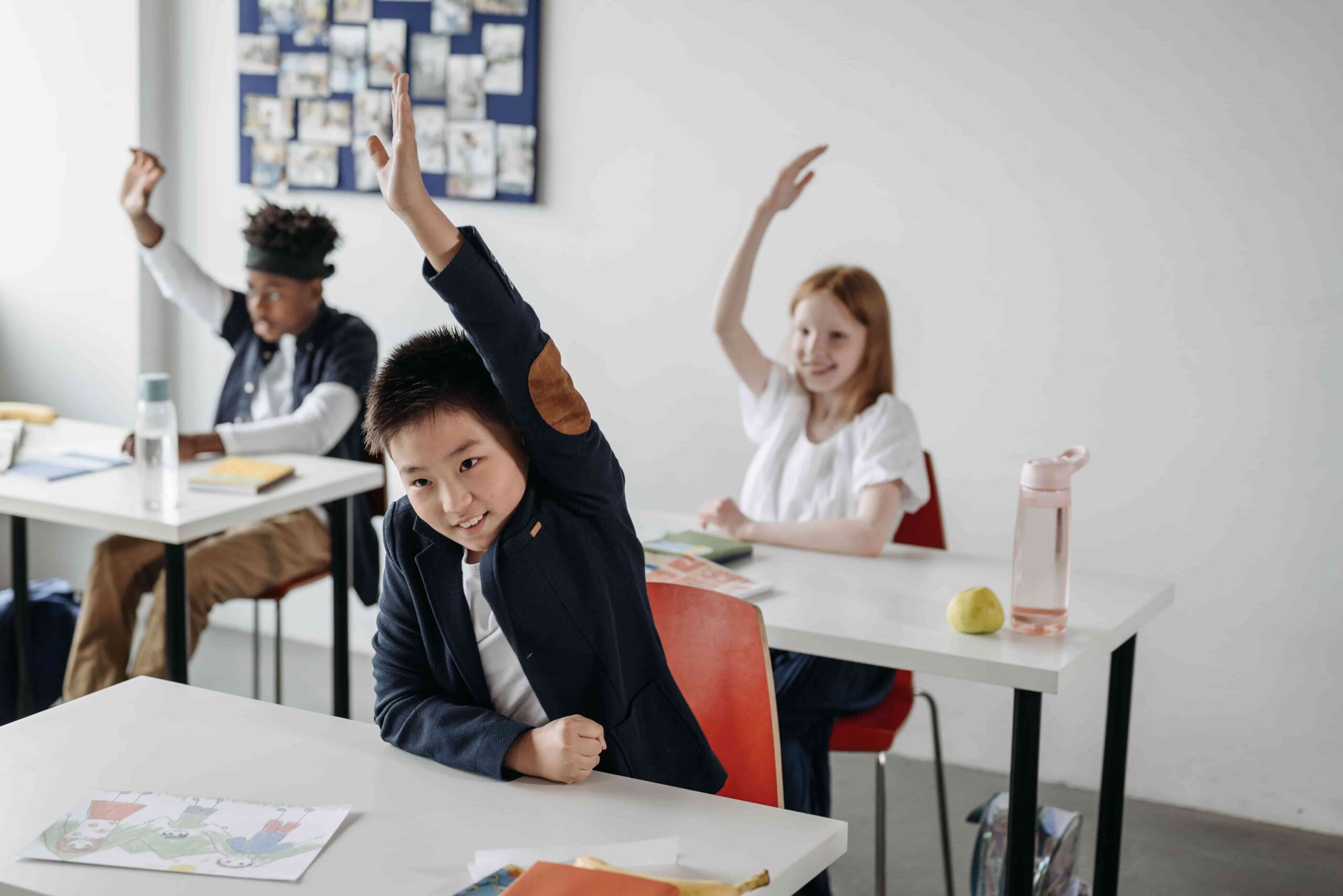 Alunos levantando a mão durante uma aula em sala de aula, ilustrando o aprendizado da língua portuguesa e a diferença entre a fim ou afim, uma das dúvidas mais comuns de ortografia e gramática.