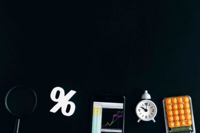 Elementos relacionados à matemática financeira, como símbolo de porcentagem, calculadora, relógio e gráfico em smartphone, ilustrando Como calcular porcentagem de forma prática para resolver descontos, aumentos e cálculos do dia a dia.