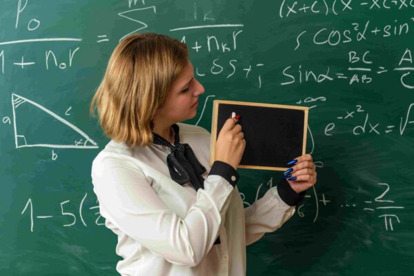 Professora explicando o Teorema de Pitágoras em sala de aula, com fórmulas matemáticas e triângulo retângulo no quadro.