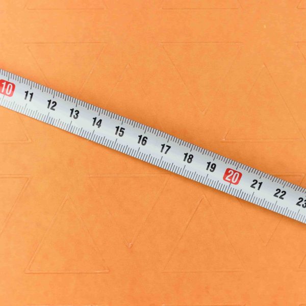 Régua metálica sobre superfície laranja representando medidas e dimensões, ilustrando conceitos de largura, comprimento e altura em unidades de medida.