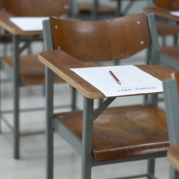 Mesa escolar com uma papel e lápis em cima representando a redação do vestibular.