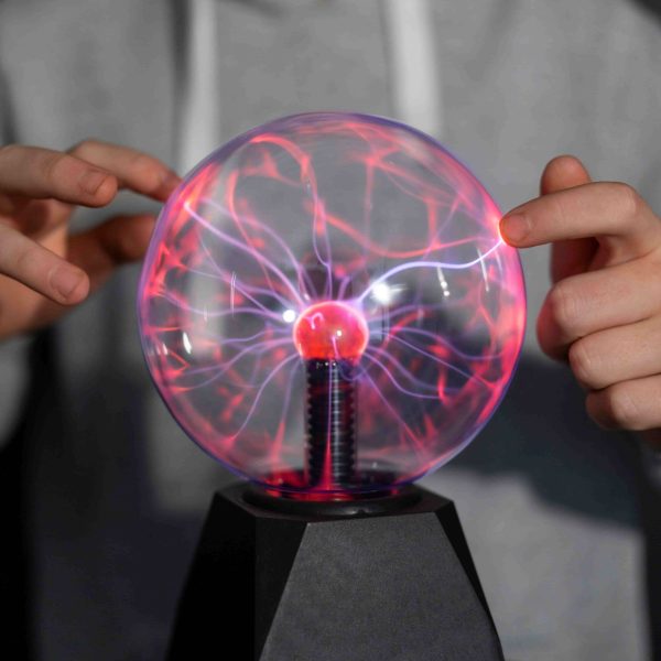 Eletromagnetismo representado por uma pessoa interagindo com uma esfera de plasma, ilustrando os fenômenos de eletricidade e magnetismo.