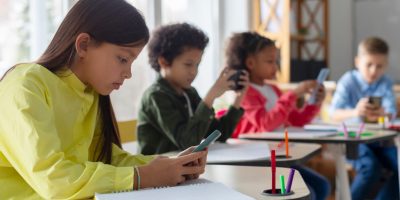 Alunos em sala de aula usando celulares e cadernos para pesquisar e estudar atualidades no Enem, desenvolvendo conhecimentos atualizados para a prova.