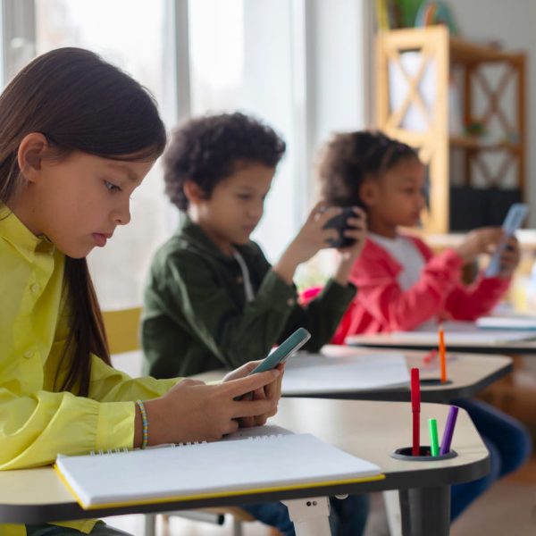 Alunos em sala de aula usando celulares e cadernos para pesquisar e estudar atualidades no Enem, desenvolvendo conhecimentos atualizados para a prova.