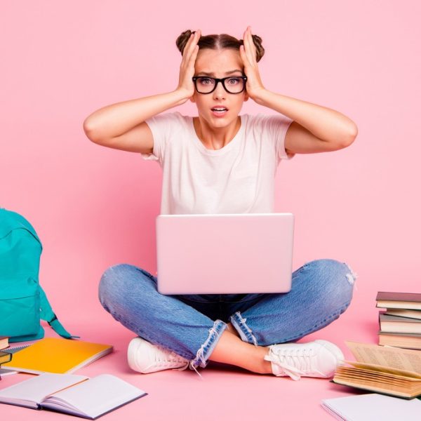 Estudante estressada com notebook e livros ao redor, representando a pressão e desafios de estudar para o vestibular e se preparar para a prova.