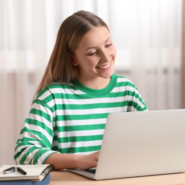 Estudante sorridente utilizando notebook para aprender como estudar por questões e aplicar o método de estudo reverso de forma eficiente.