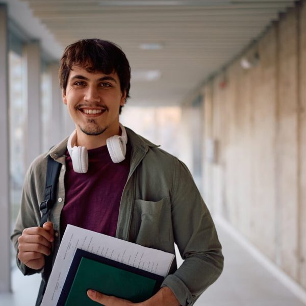 Estudante sorridente em corredor universitário com materiais de estudo, representando o período de inscrições Sisu 2026 e o acesso a vagas no ensino superior.