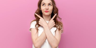 Mulher em dúvida apontando para os dois lados, com expressão pensativa, representando a confusão comum entre as palavras mal ou mau na língua portuguesa.