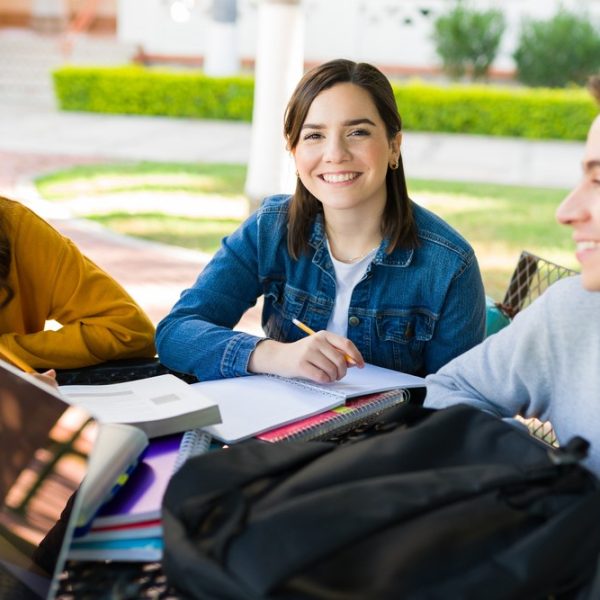 Grupo de estudantes estudando ao ar livre para o Vestibular Unicamp, com livros, cadernos e notebooks.